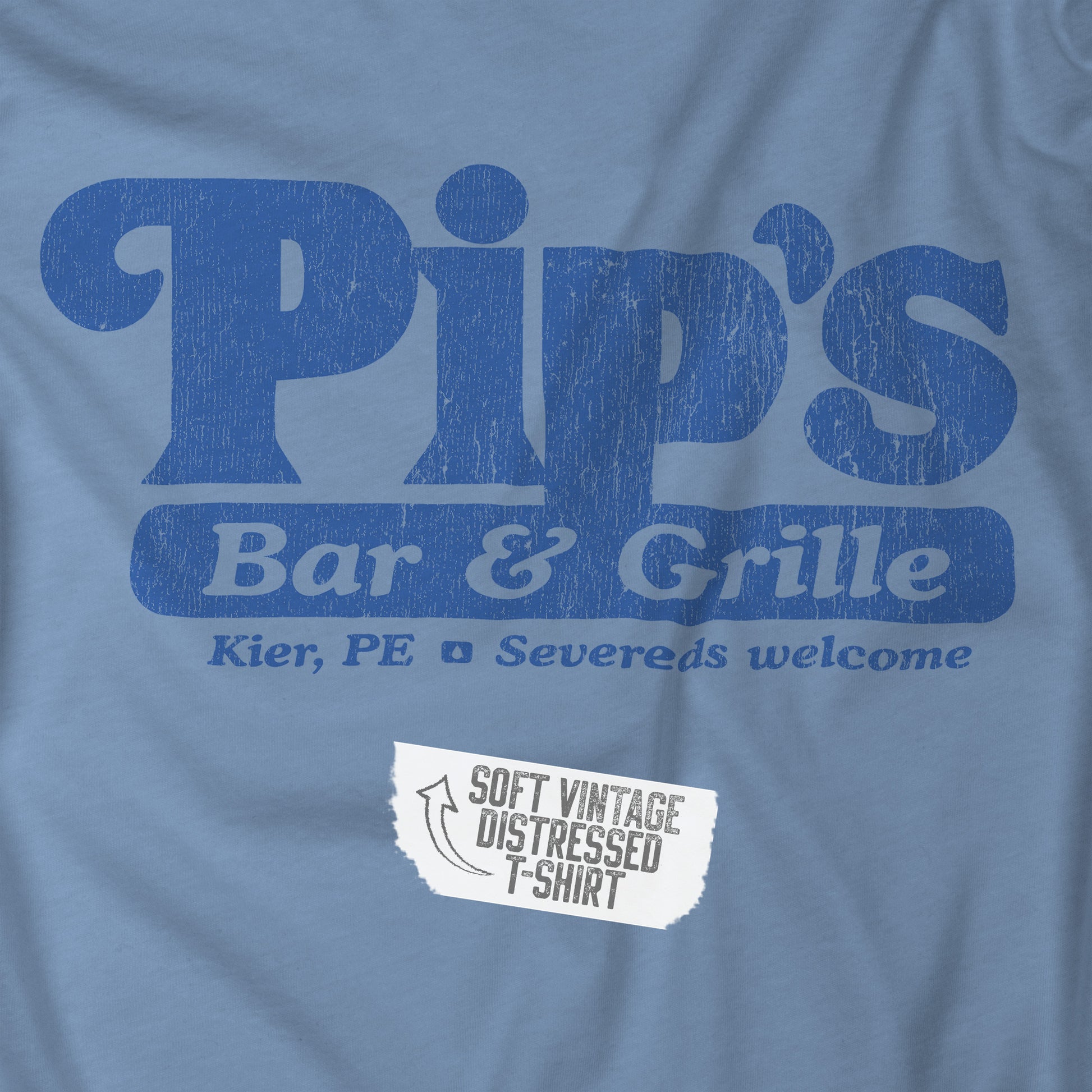 Closeup of a steel blue colored soft Bella+Canvas shirtsleeve t-shirt with the Pips Bar and Grill logo from the TV show Severance in a vintage distressed ink-stamped worn-in style.