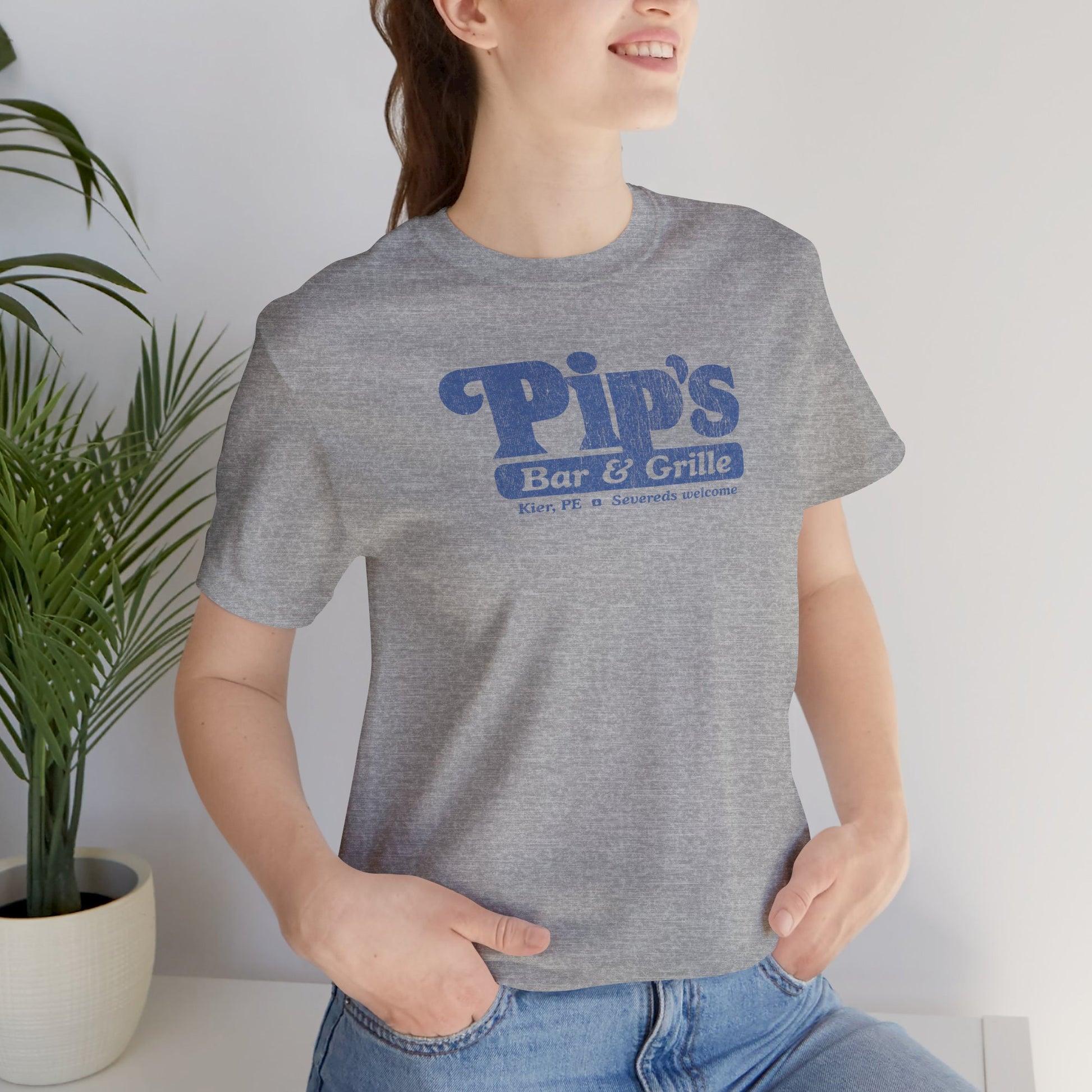 Woman wearing heather grey Bella+Canvas t-shirt with the Pips Bar and Grill logo from the TV show Severance in a vintage distressed style.