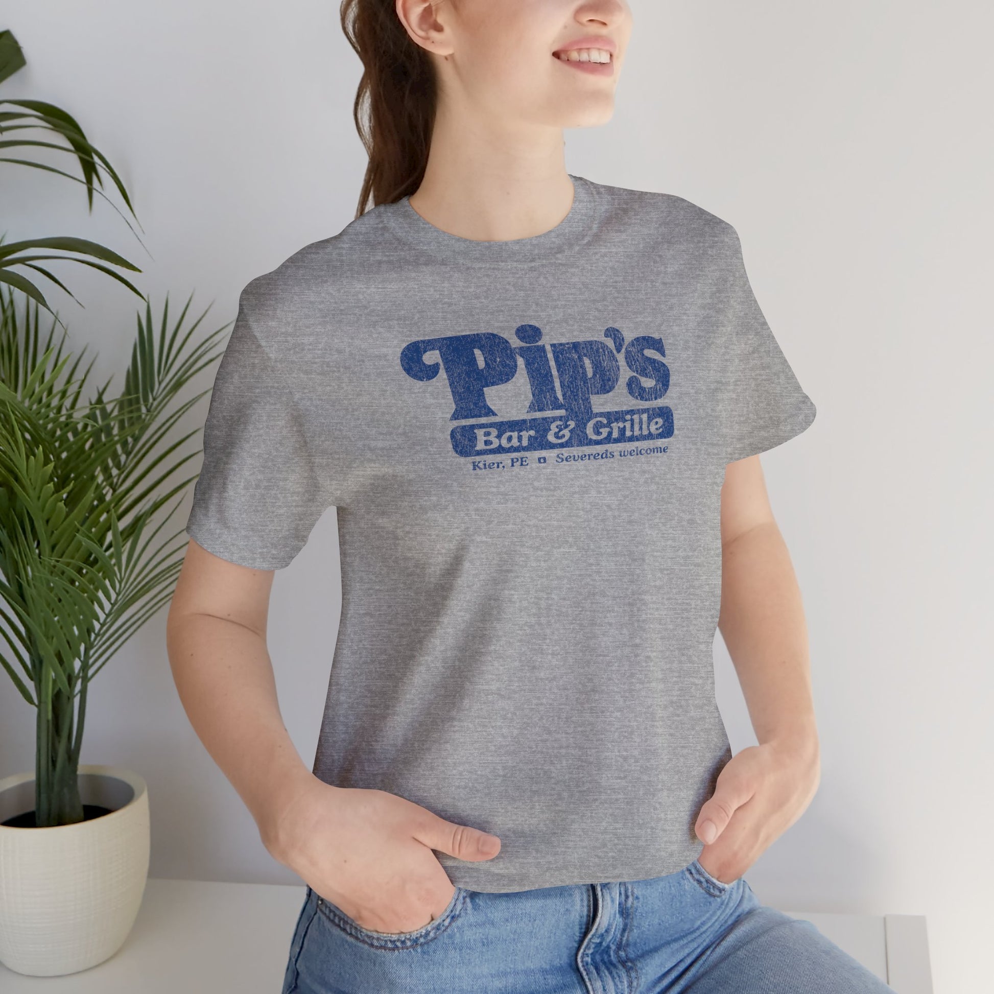 Woman wearing heather grey Bella+Canvas t-shirt with the Pips Bar and Grill logo from the TV show Severance in a vintage distressed style.