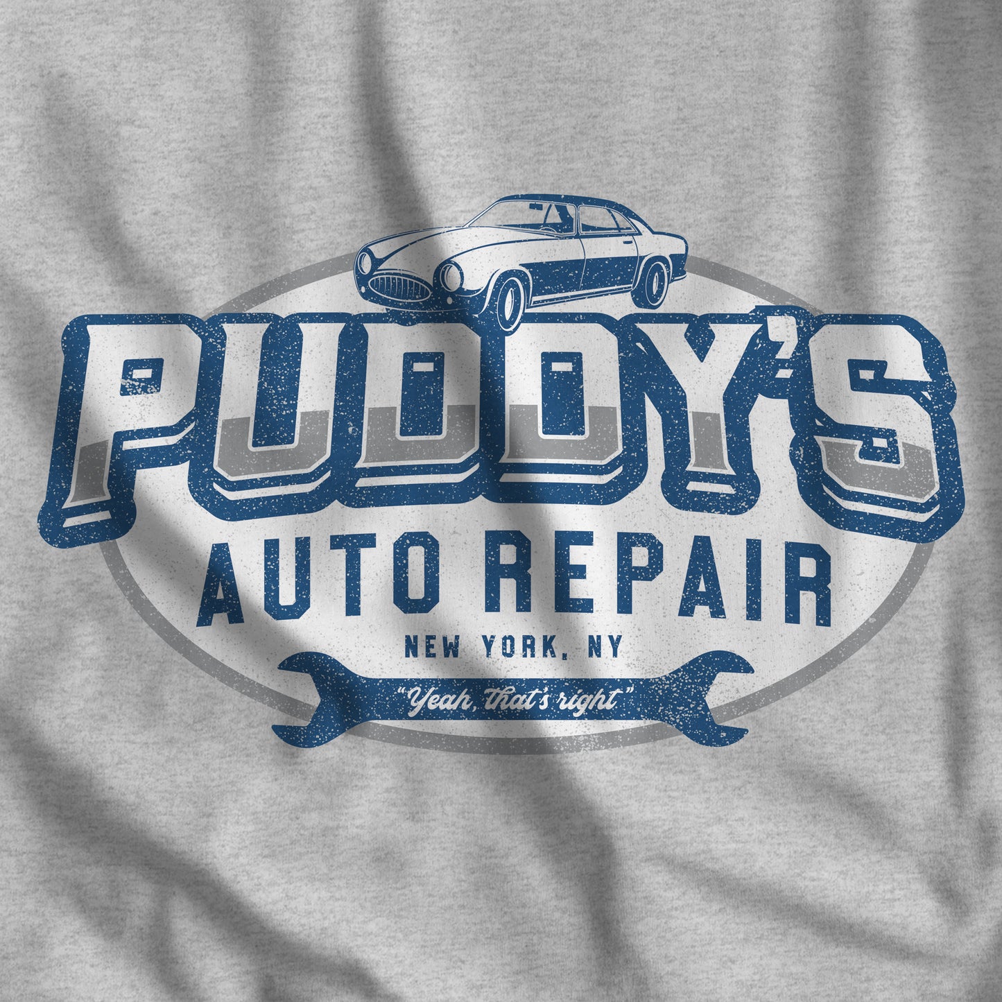 Closeup of heather grey t-shirt with a Puddy's Auto Repair graphic inspired by Seinfeld, in a vintage distressed style.