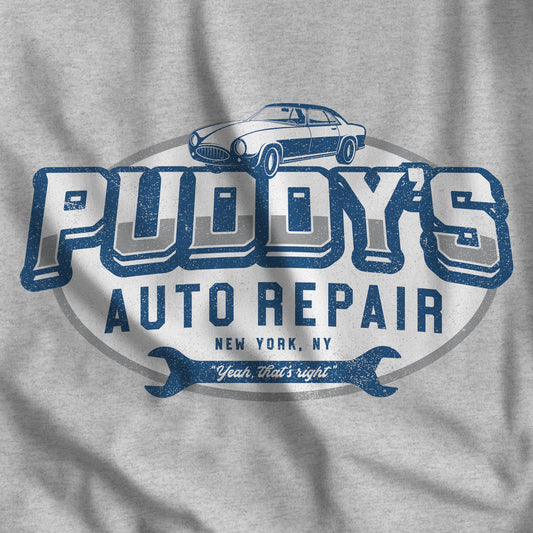 Closeup of heather grey t-shirt with a Puddy's Auto Repair graphic inspired by Seinfeld, in a vintage distressed style.