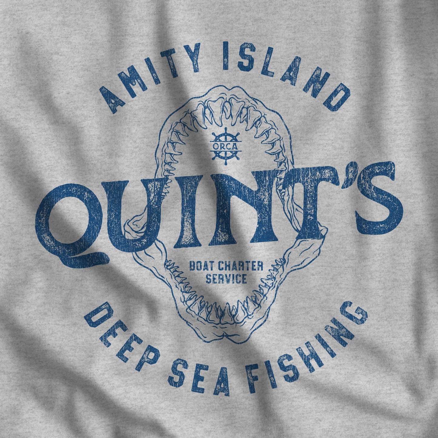 Closeup of t-shirt featuring the Quint's Deep Sea Fishing Boat Charters logo graphic inspired by the movie Jaws in a vintage distressed style.