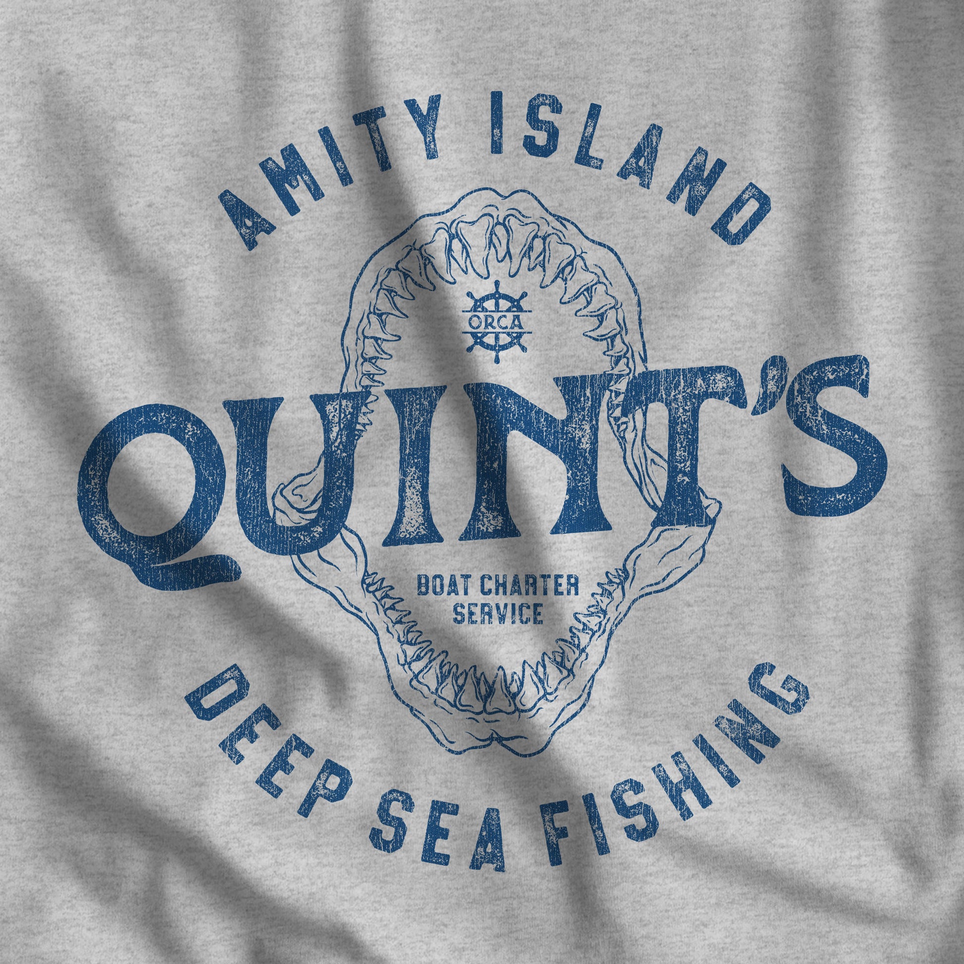 Closeup of t-shirt featuring the Quint's Deep Sea Fishing Boat Charters logo graphic inspired by the movie Jaws in a vintage distressed style.