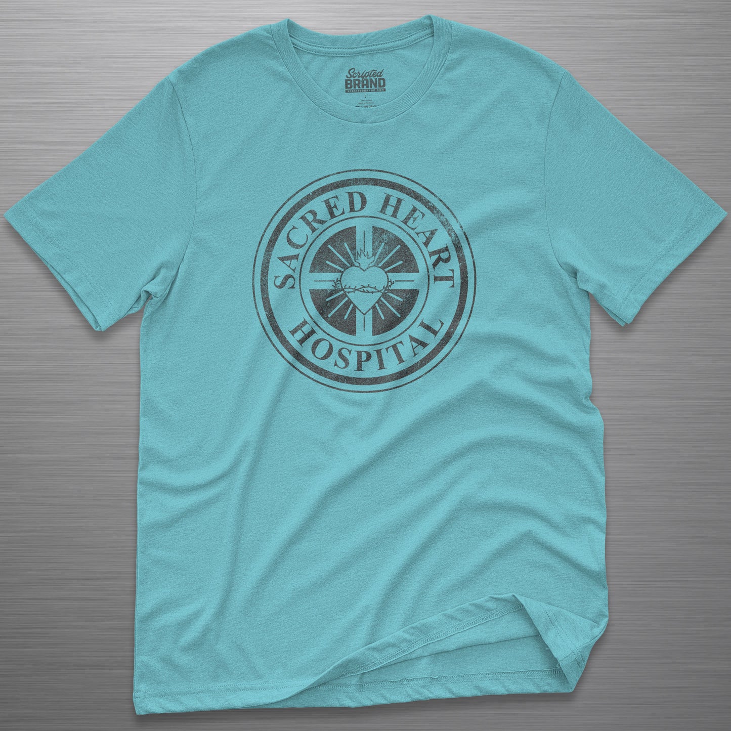 Turquoise blue Bella Canvas 3001 tee with vintage distressed Sacred Heart Hospital logo from Scrubs printed on chest, shown on a metal table.