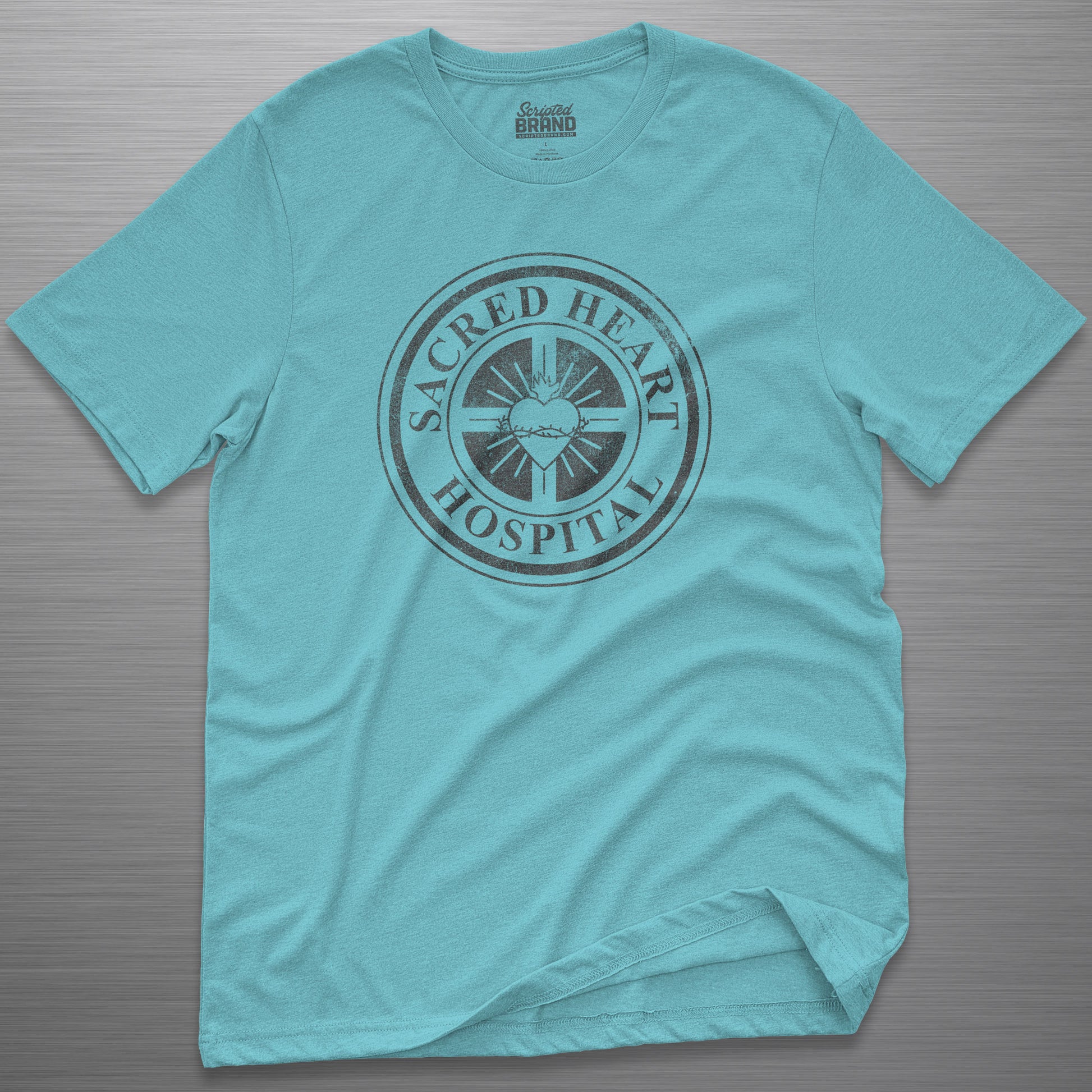 Turquoise blue Bella Canvas 3001 tee with vintage distressed Sacred Heart Hospital logo from Scrubs printed on chest, shown on a metal table.
