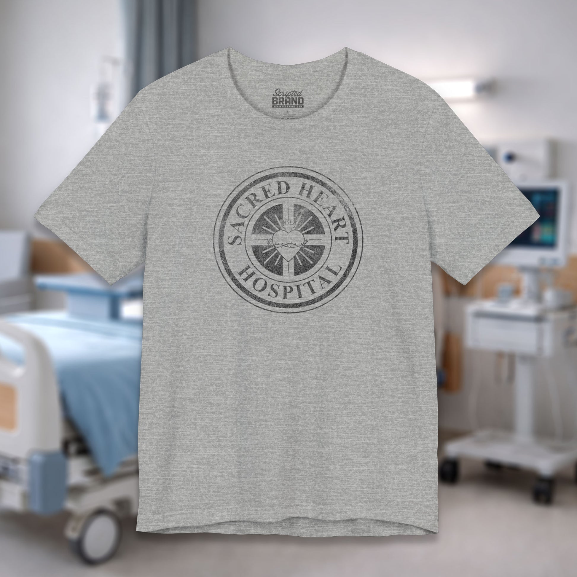 Heather gray Bella Canvas 3001 tee with vintage distressed Sacred Heart Hospital logo from Scrubs printed on chest, shown in a hospital.