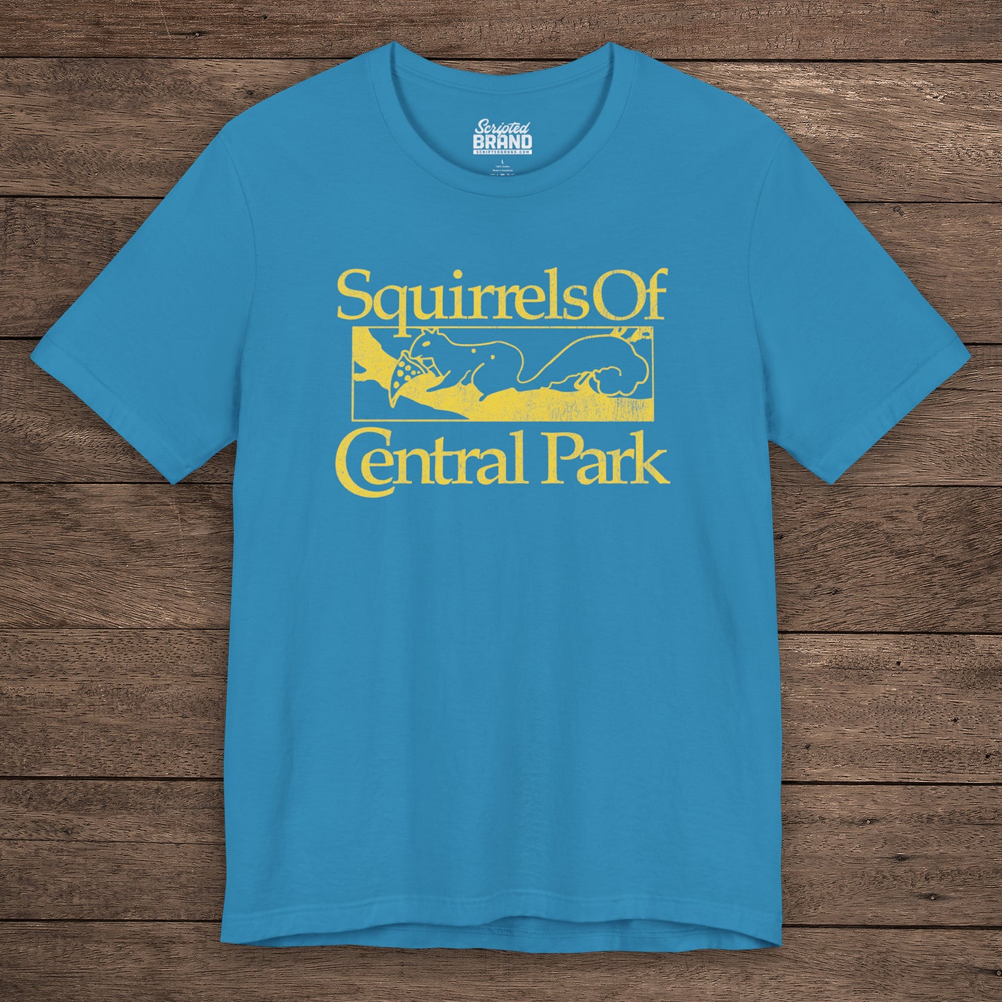 Aqua blue unisex t-shirt with distressed yellow “Squirrels of Central Park” graphic, worn by Eva Garvey in the show Bad Sisters.