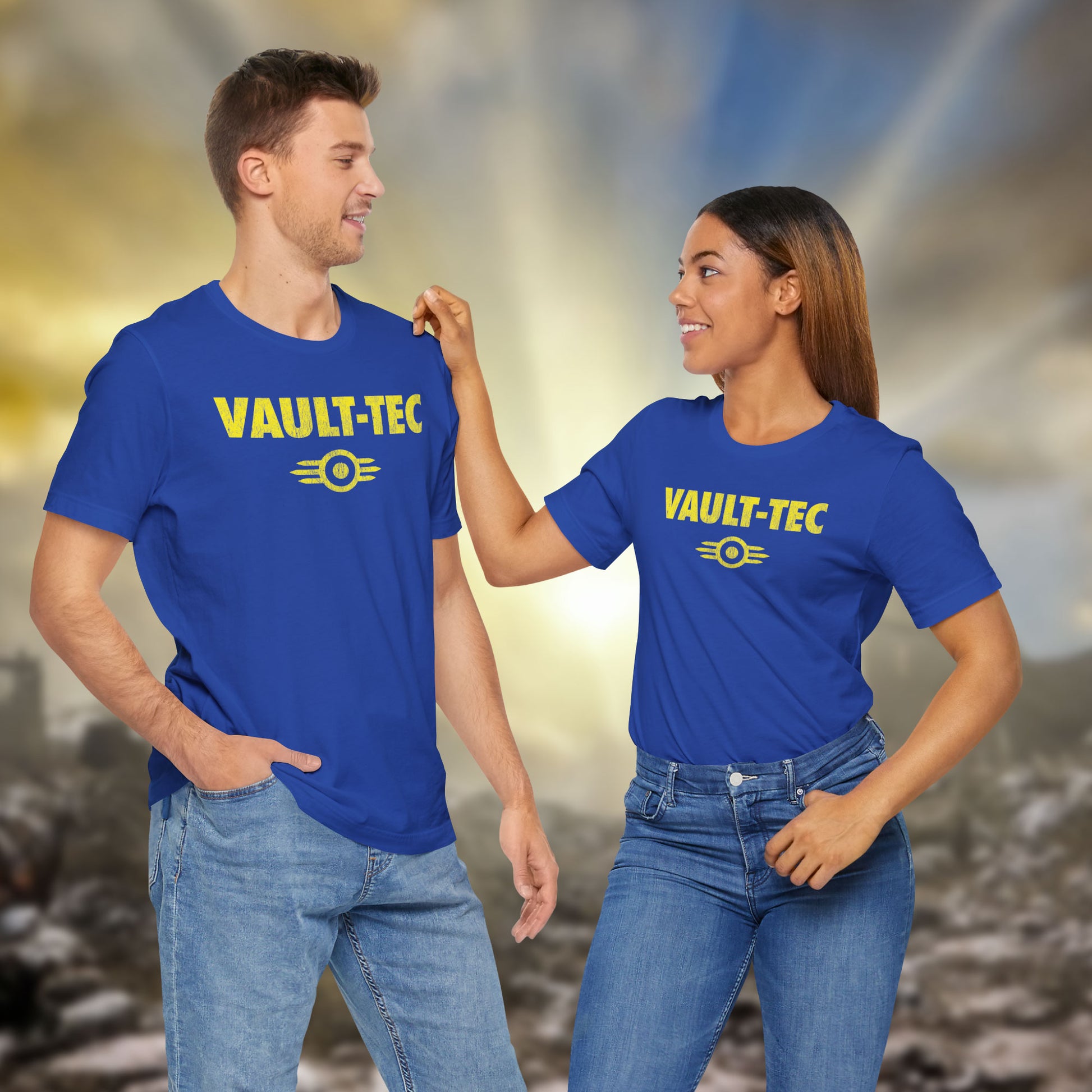 Two people wearing royal blue t-shirts featuring the Vault-Tec logo graphic from the video game Fallout in a vintage distressed style. 