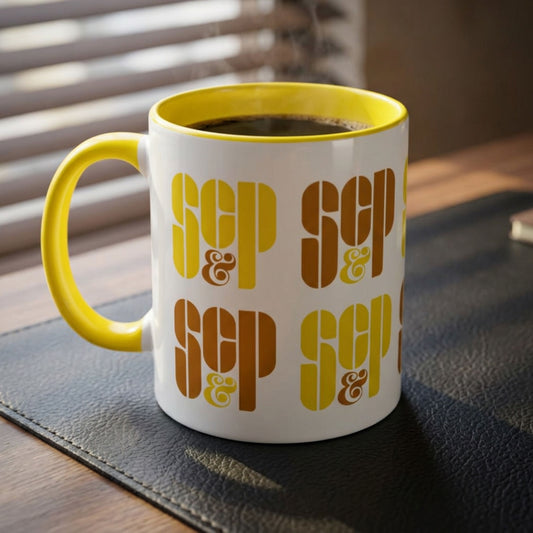 Mad Men white and yellow ceramic mug with a wraparound graphic of Sterling Cooper & Partners logos, on a desk.
