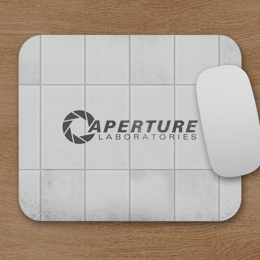 Mouse pad featuring Aperture Laboratories logo with a grungy panel wall texture design, shown with mouse on a desk.
