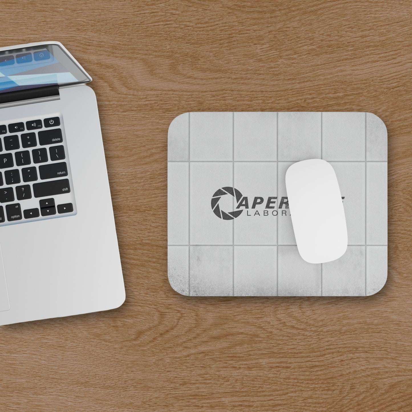 Topdown view of a mouse pad featuring Aperture Laboratories logo with a grungy panel wall texture design, shown with mouse and computer on a desk.