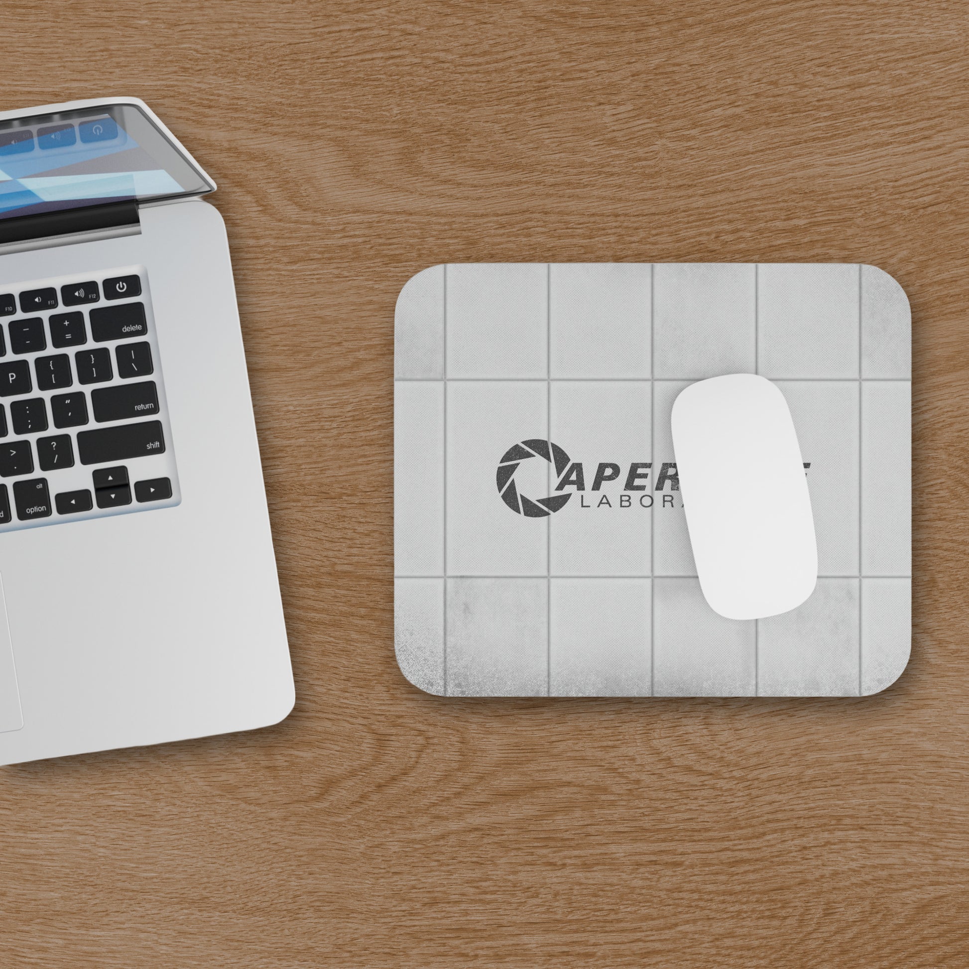 Topdown view of a mouse pad featuring Aperture Laboratories logo with a grungy panel wall texture design, shown with mouse and computer on a desk.