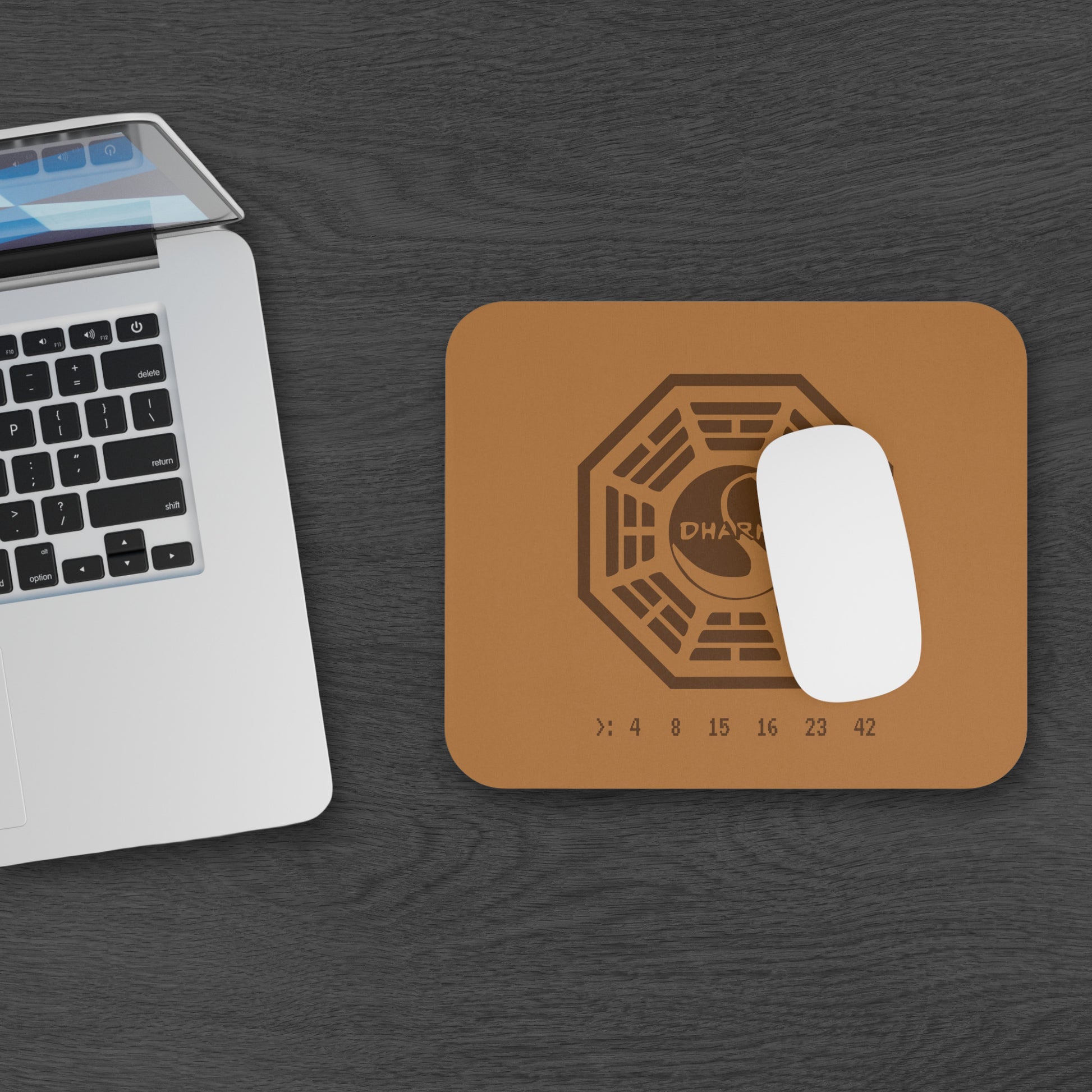 Topdown view of tan 9x8 mouse pad with Dharma Initiative Swan Station logo and hatch numbers from TV show Lost, on a desk with a computer and mouse
