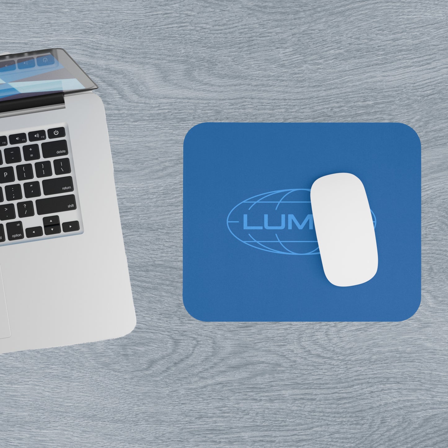 Top down view of a 9x8 modern blue Mouse pad with the Lumon Industries logo from the TV show Severance, next to a MacBook.
