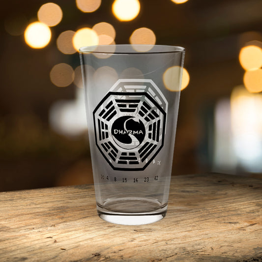 Clear 16 oz pint glass with Dharma Initiative Swan Station logo and hatch numbers from Lost Show, on a bar table