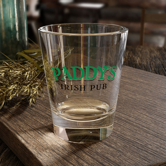 1.5 oz clear Paddy’s Pub shot glass with green logo inspired by It’s Always Sunny in Philadelphia, shown on a table.