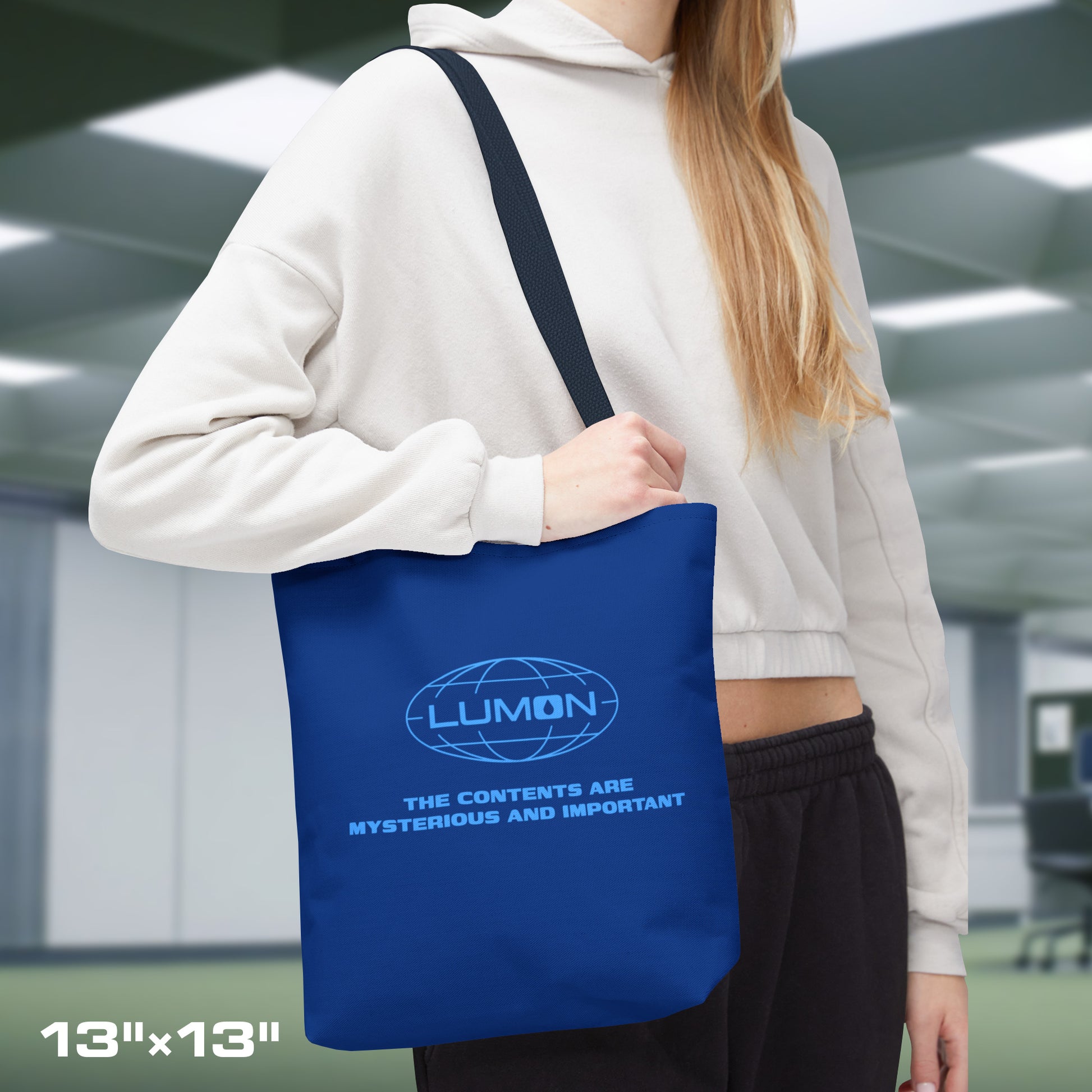 Female model carrying a 13" x 13" Blue Tote Bag featuring the logo of Lumon Industries from the Apple TV Show Severance, along with added customizable text by the customer, which is "THE CONTENTS ARE MYSTERIOUS AND IMPORTANT."