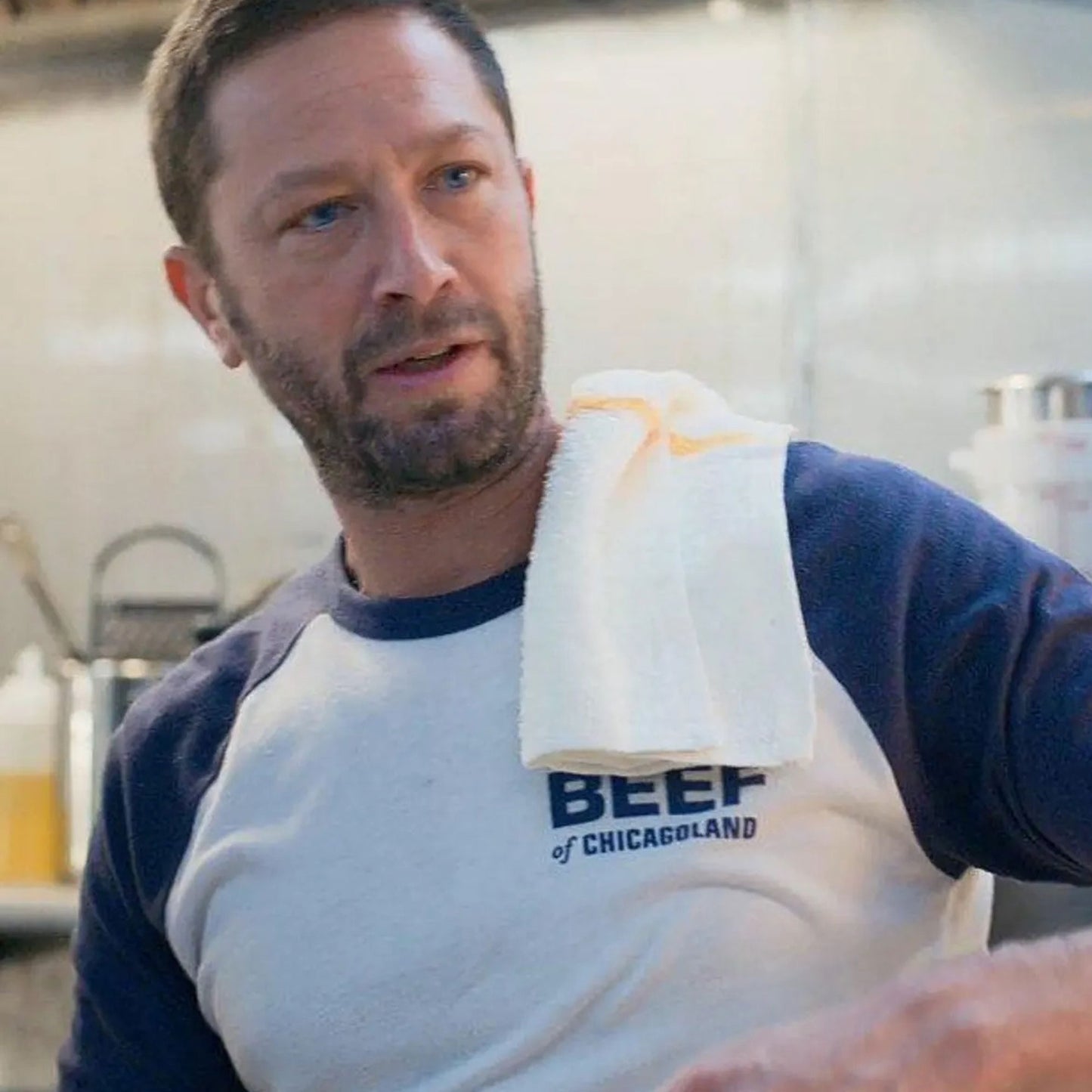Scene from The Bear, Richie wearing Original Beef of Chicagoland raglan baseball t-shirt, white body with navy blue 3/4 sleeves and chest logo.
