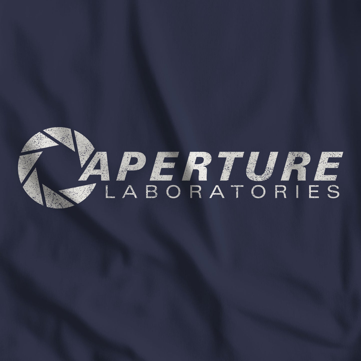 Closeup of Navy blue Bella Canvas t-shirt with the Aperture Laboratories logo from the video game Portal and Portal 2 in a vintage distressed style.