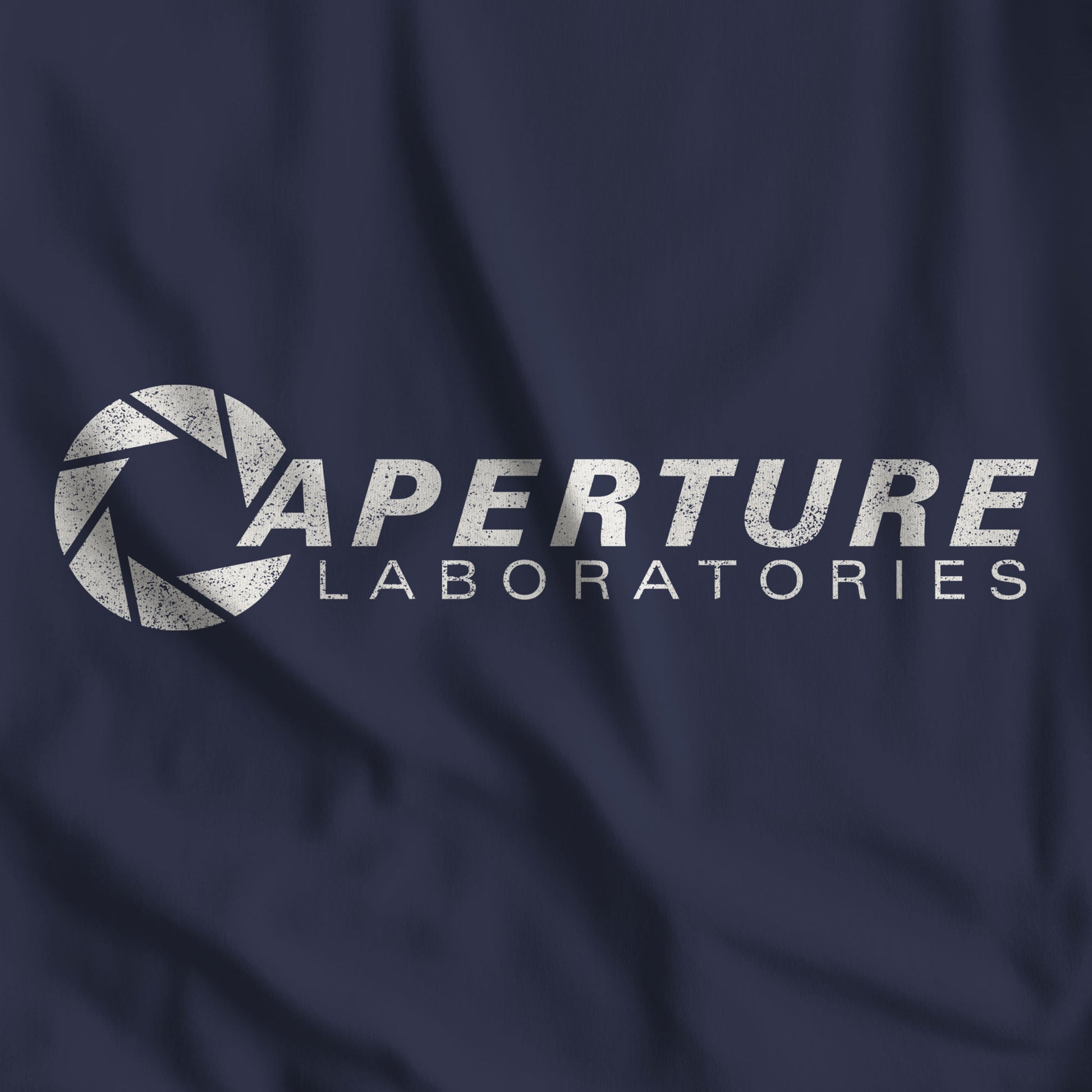 Closeup of Navy blue Bella Canvas t-shirt with the Aperture Laboratories logo from the video game Portal and Portal 2 in a vintage distressed style.