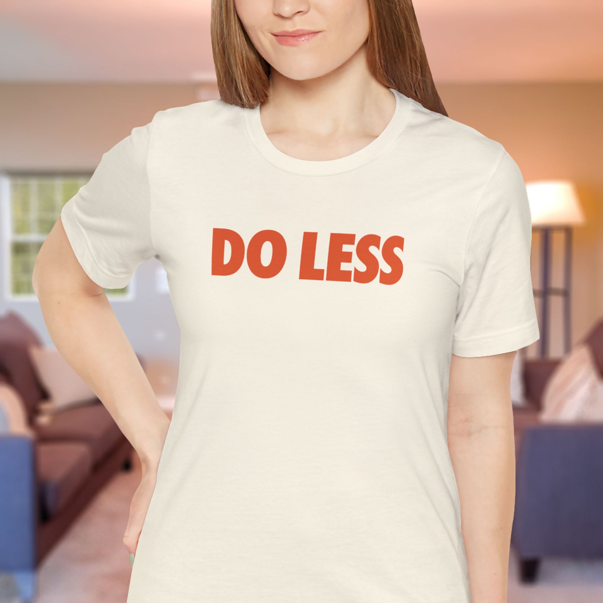 Woman wearing Natural Off-white Do Less graphic t-shirt inspired by Shrinking TV show, Bella+Canvas cotton tee with orange type