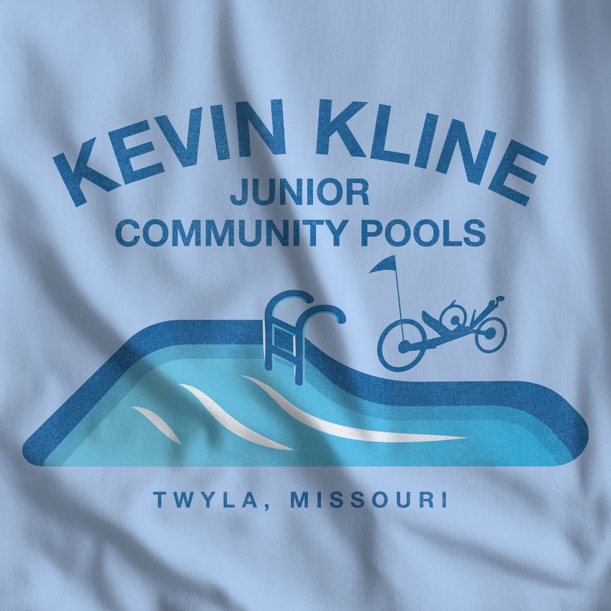 Closeup of DTF St. Louis Kevin Kline Junior Community Pools graphic tee with pool and recumbent trike, Bella+Canvas 3001 Light blue.