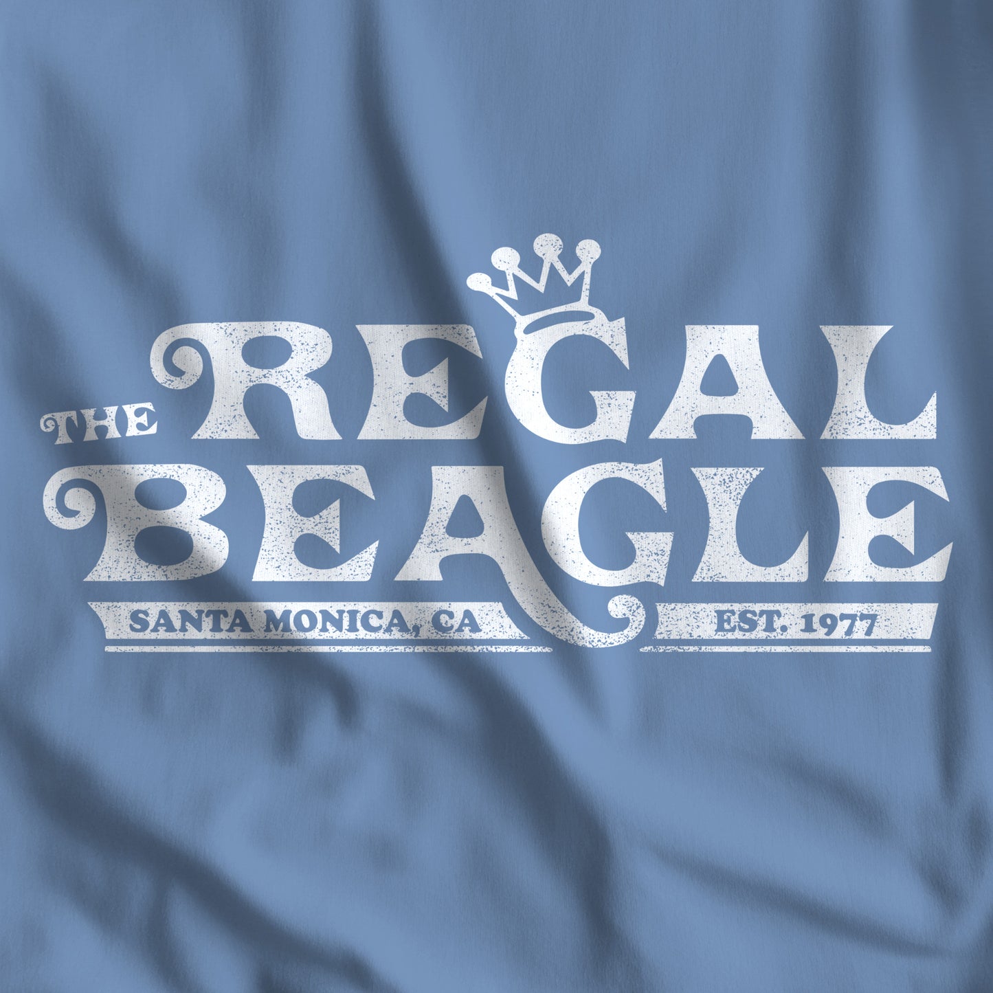 Closeup of Lavender Blue Bella+Canvas t-shirt with the Regal Beagle logo from the TV Show 'Threes Company' in a vintage distressed style.