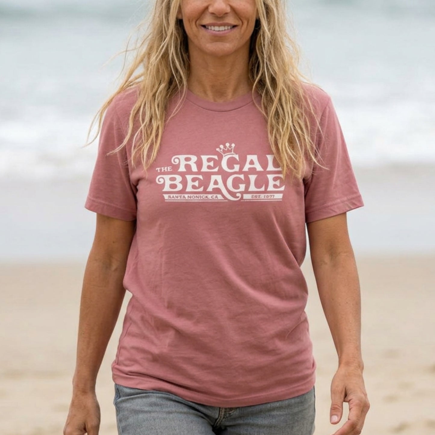 Person wearing Mauve Bella+Canvas t-shirt with the Regal Beagle logo from the TV Show 'Threes Company' in a vintage distressed style.