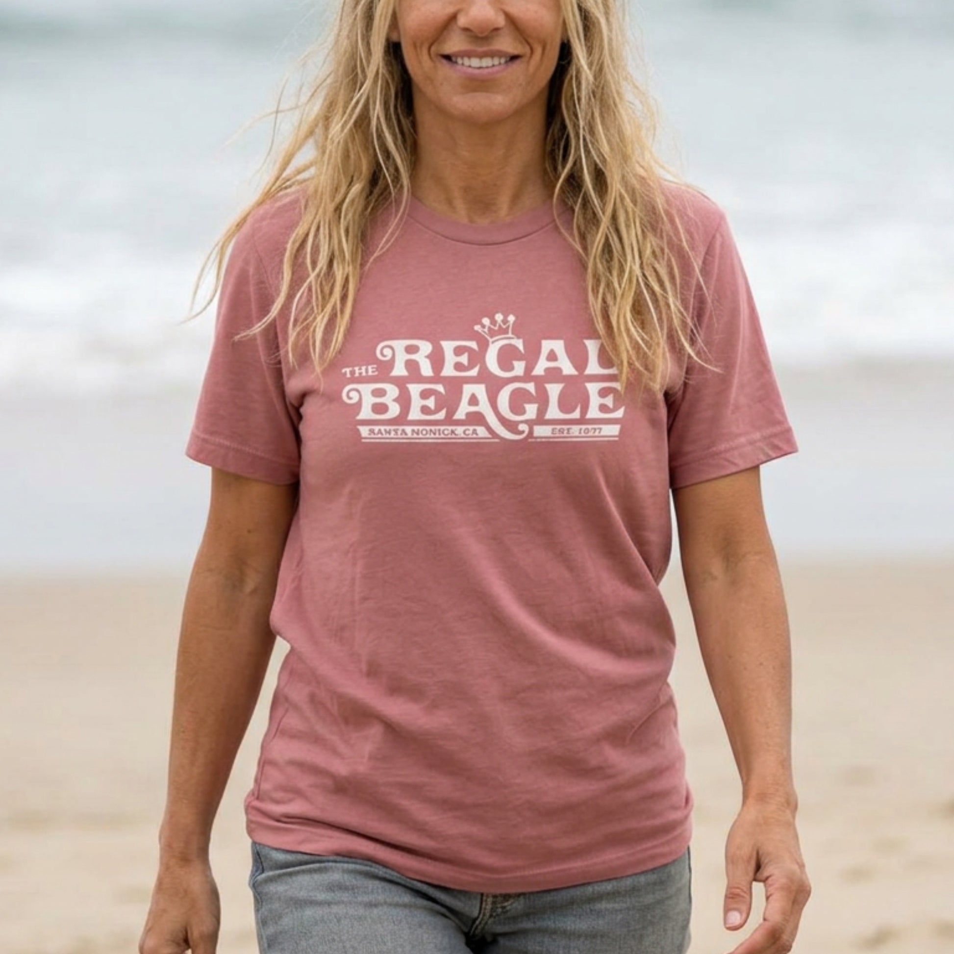 Person wearing Mauve Bella+Canvas t-shirt with the Regal Beagle logo from the TV Show 'Threes Company' in a vintage distressed style.