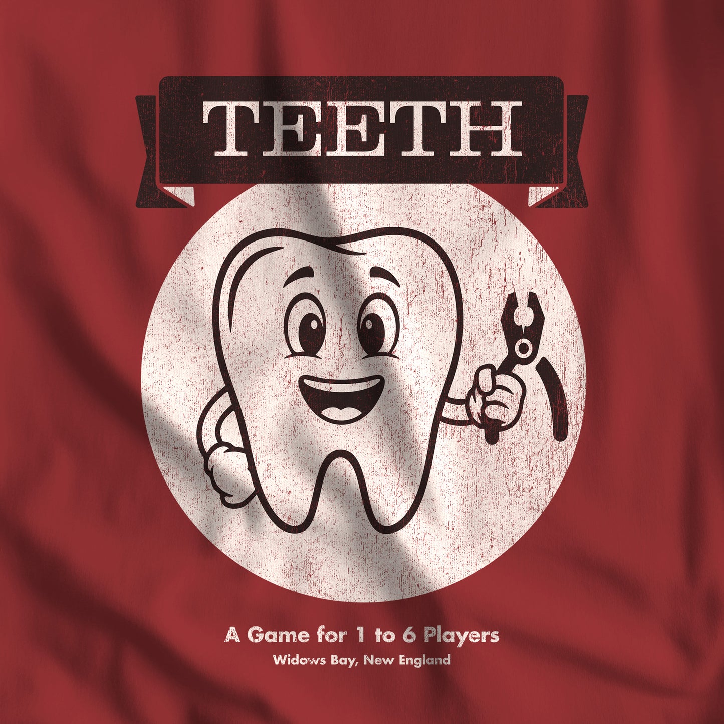 Closeup of Cardinal Red Bella+Canvas tee with the vintage TEETH board game box cover from Widow's Bay, a smiling tooth holding pliers