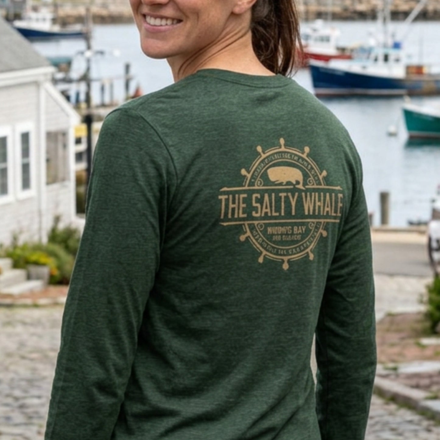 Back of person wearing Heather forest green long sleeve tee with vintage gold The Salty Whale logos from the TV show Widow's Bay nautical on front and back