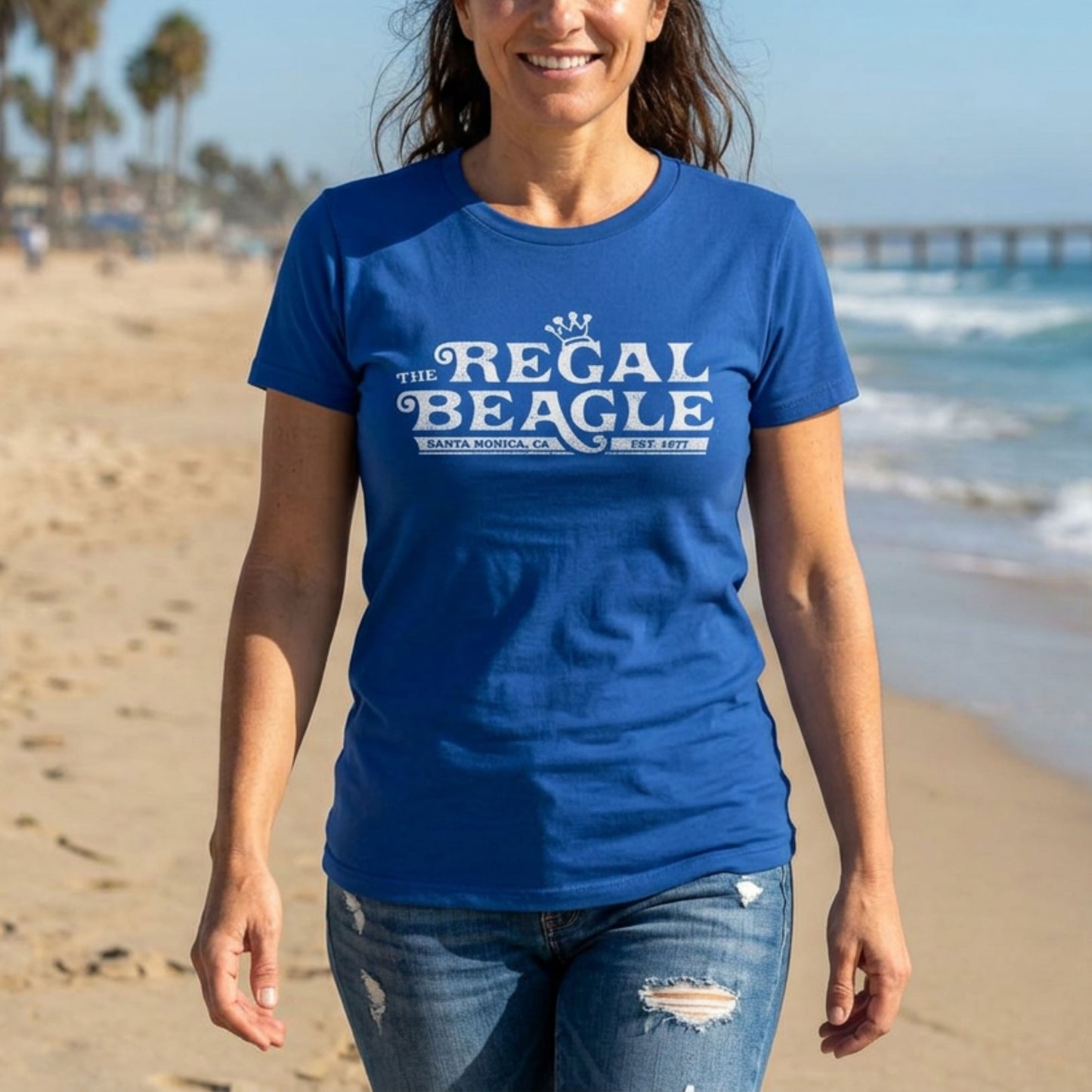 Woman on a beach wearing royal blue womens boyfriend tee with vintage distressed Regal Beagle Three's Company logo