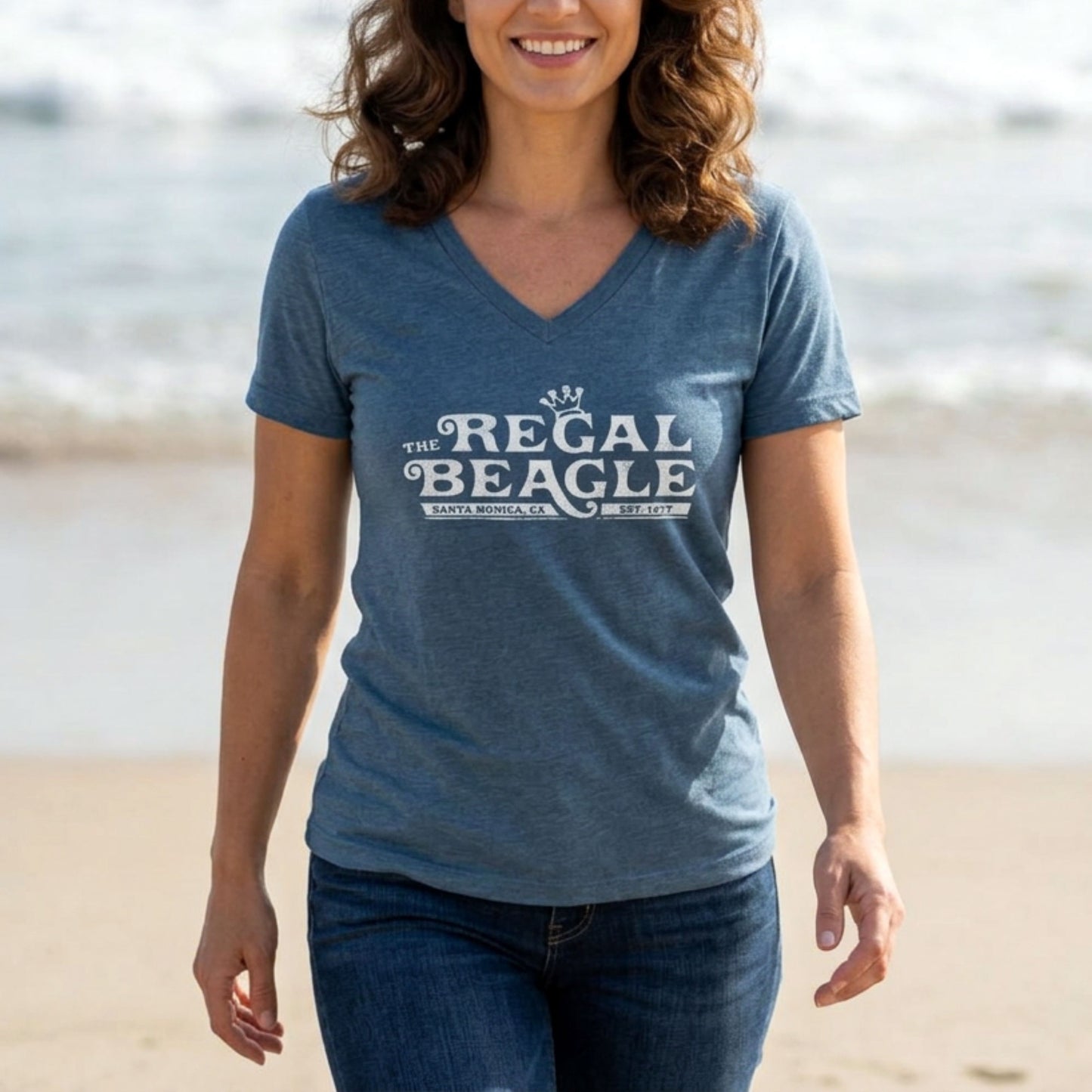 Person wearing Heather slate blue womens v-neck tee with vintage distressed Regal Beagle Three's Company logo