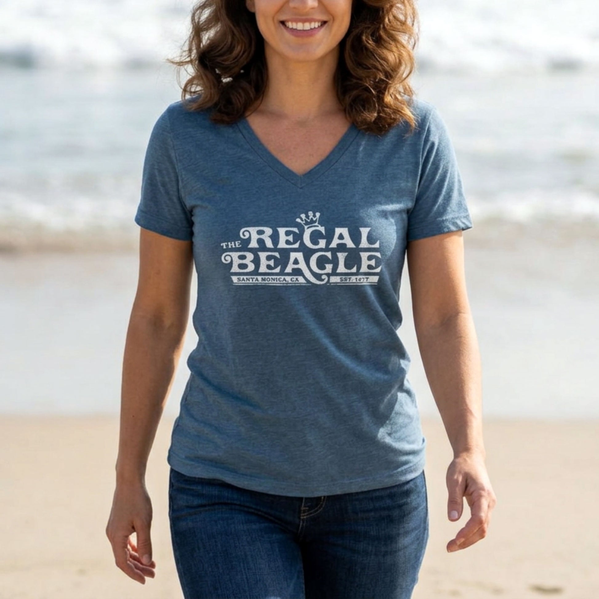 Person wearing Heather slate blue womens v-neck tee with vintage distressed Regal Beagle Three's Company logo