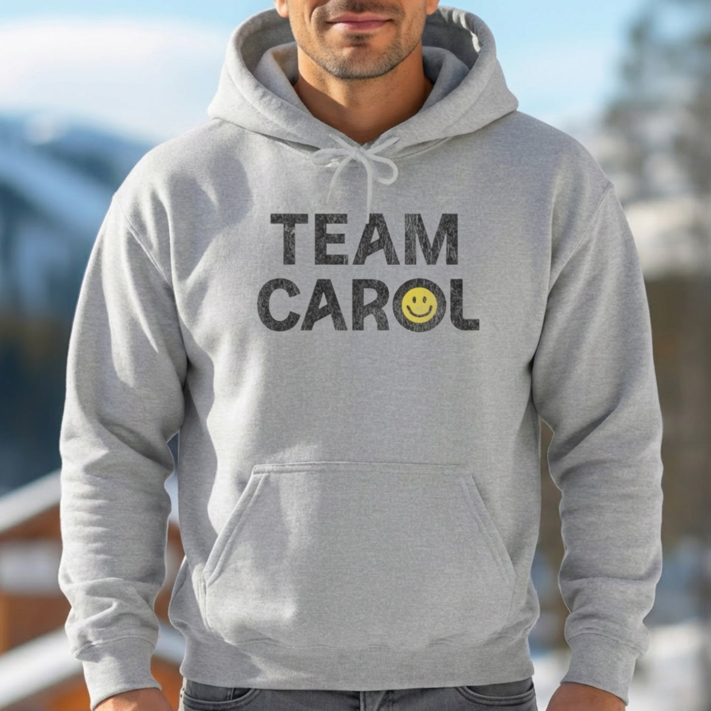 Man wearing heather gray unisex Heavy Blend pullover hoodie sweatshirt with TEAM CAROL vintage distressed smiley graphic