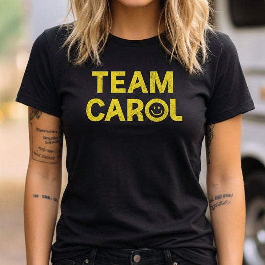 Woman wearing Black TEAM CAROL t-shirt inspired by Pluribus with vintage distressed smiley face graphic in yellow