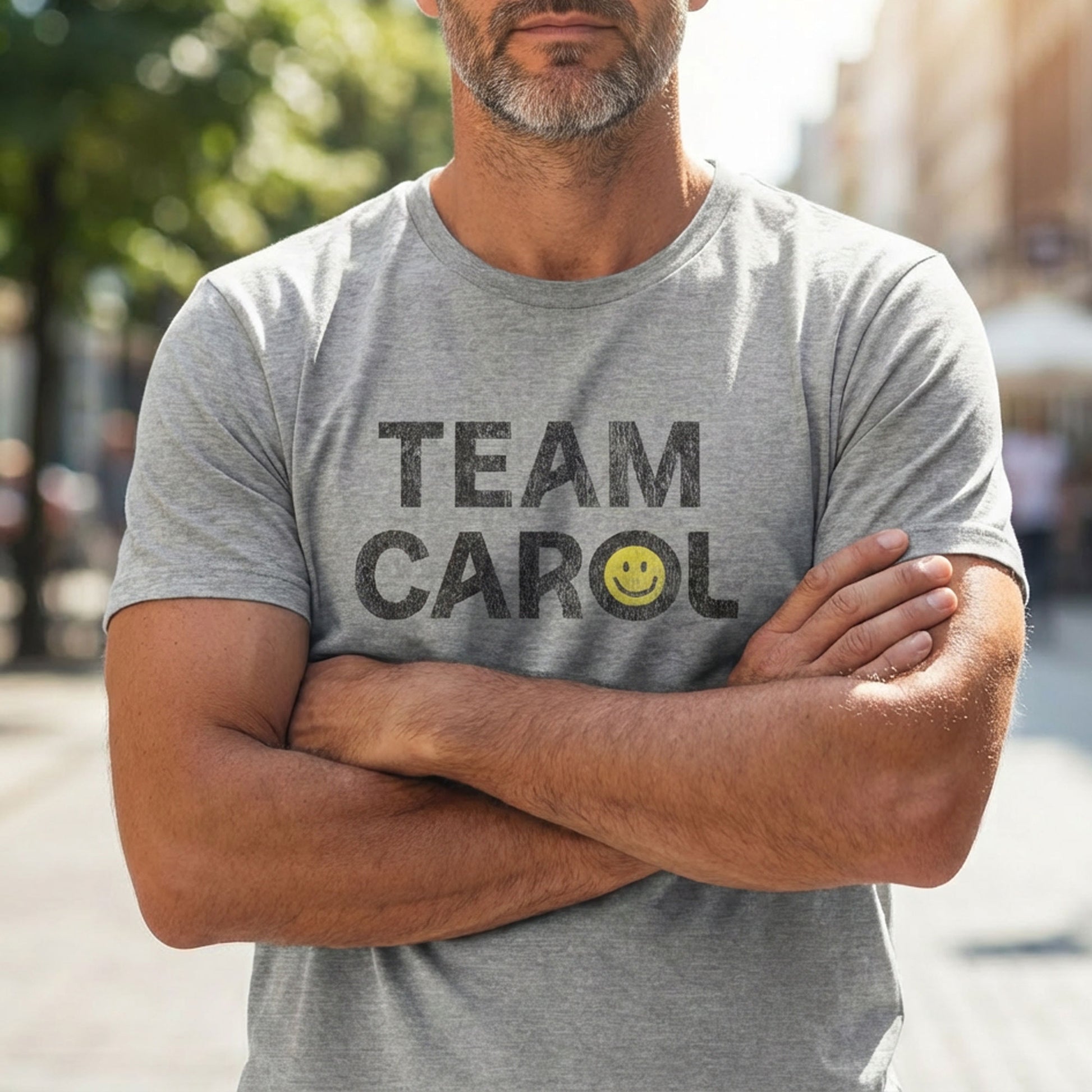 Man wearing heather gray TEAM CAROL t-shirt inspired by Pluribus with vintage distressed smiley face graphic in black