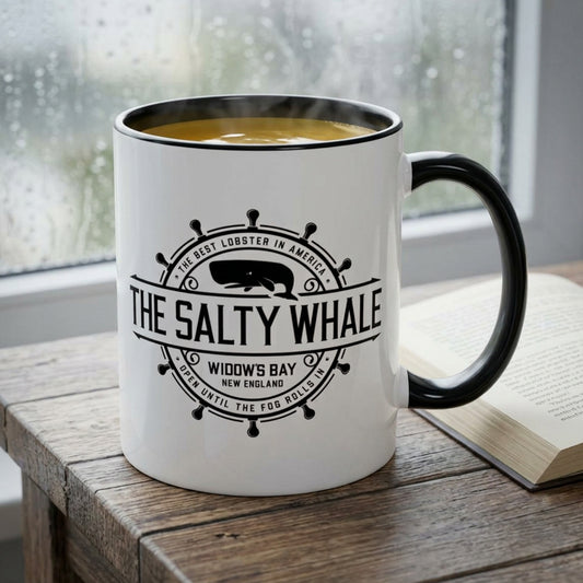 White ceramic mug with black handle and the vintage Salty Whale maritime crest logo from Widow's Bay TV show, on a table