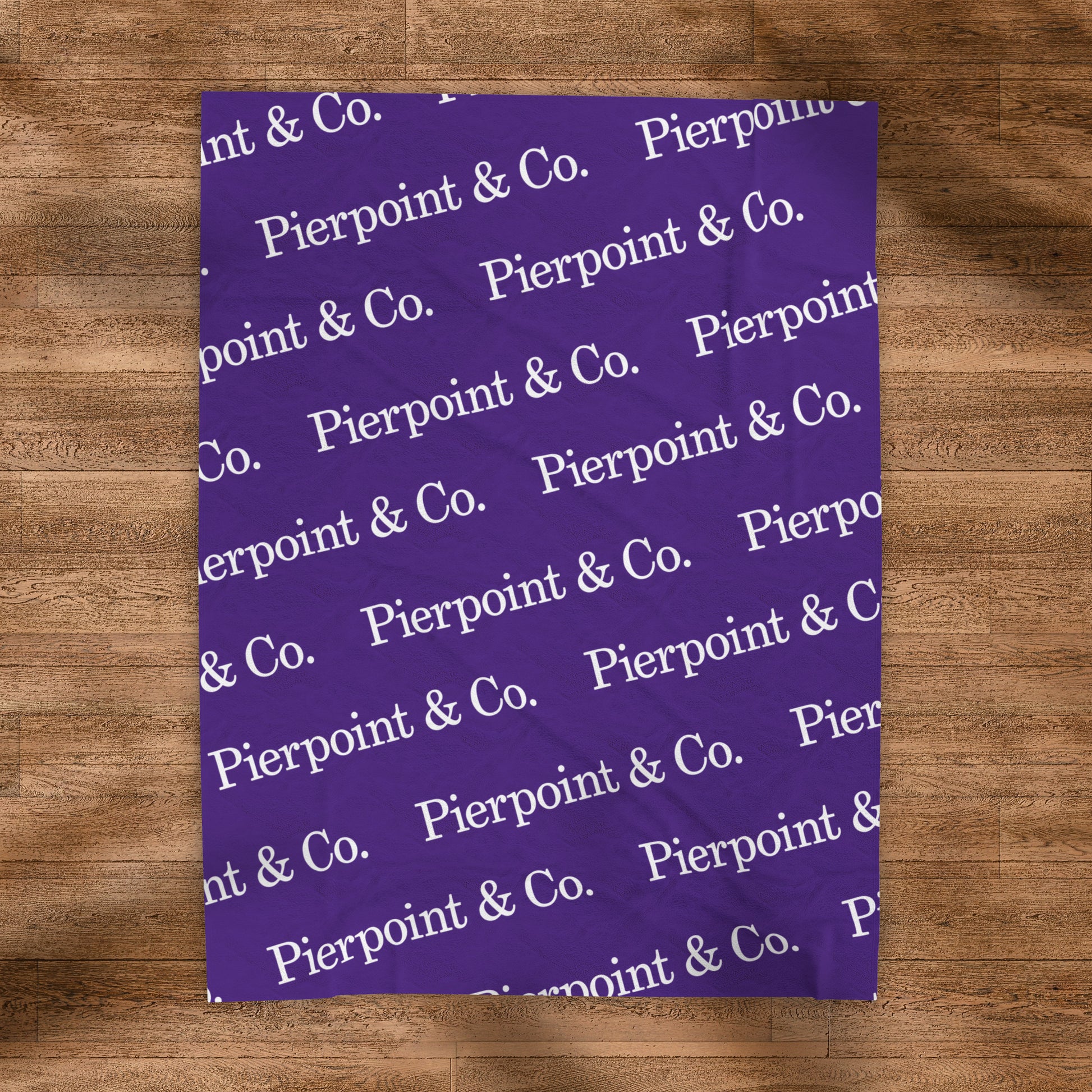 Velveteen Plush Purple Blanket with a step and repeat pattern of Pierpoint & Co. logos from the HBO TV show Industry, placed on a wood floor.