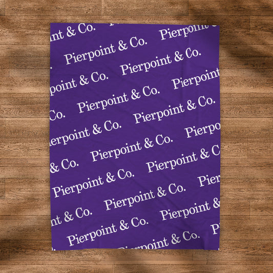 Velveteen Plush Purple Blanket with a step and repeat pattern of Pierpoint & Co. logos from the HBO TV show Industry, placed on a wood floor.