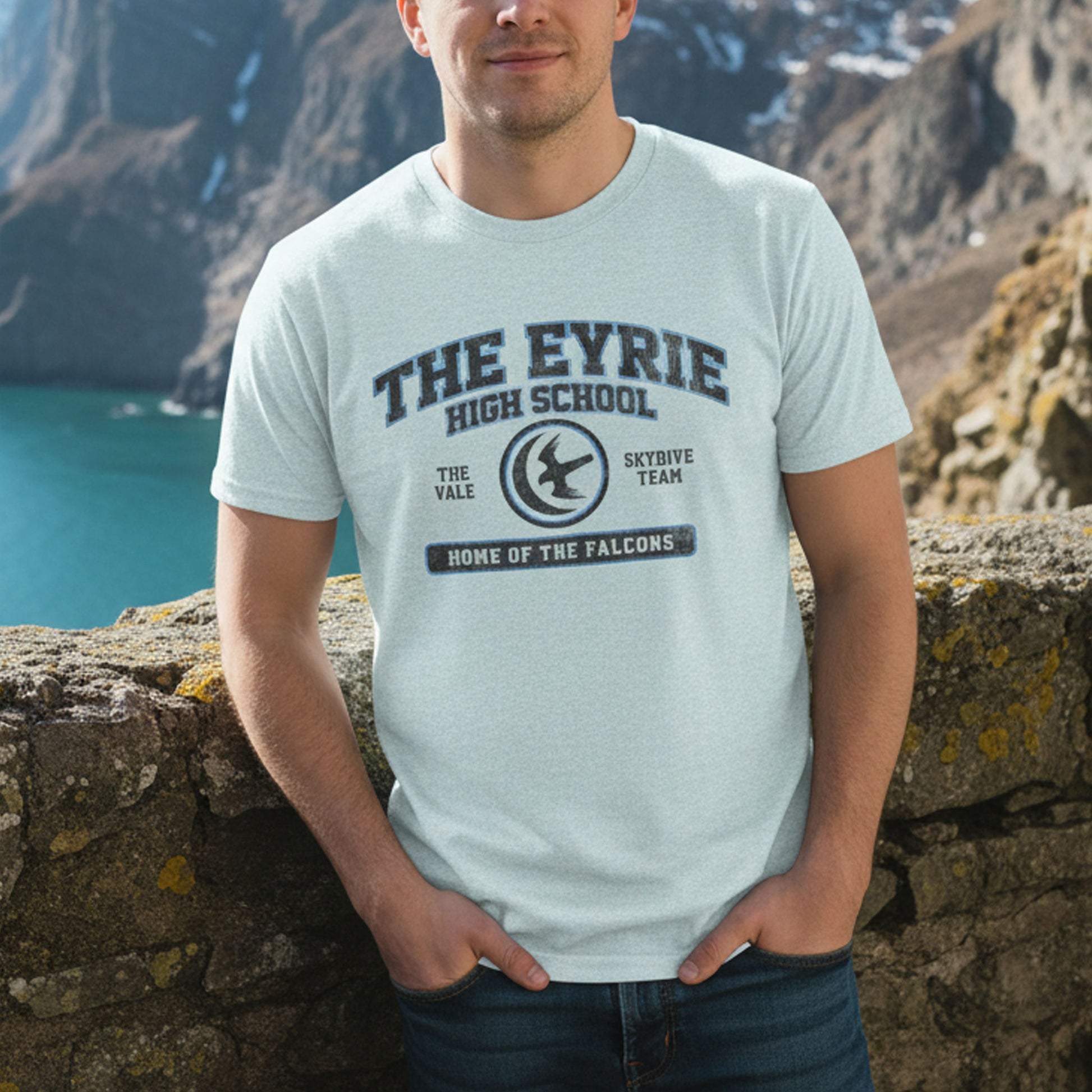 Person wearing heather prism ice blue The Eyrie High School t-shirt with vintage falcon moon door graphic inspired by Game of Thrones and the Vale.