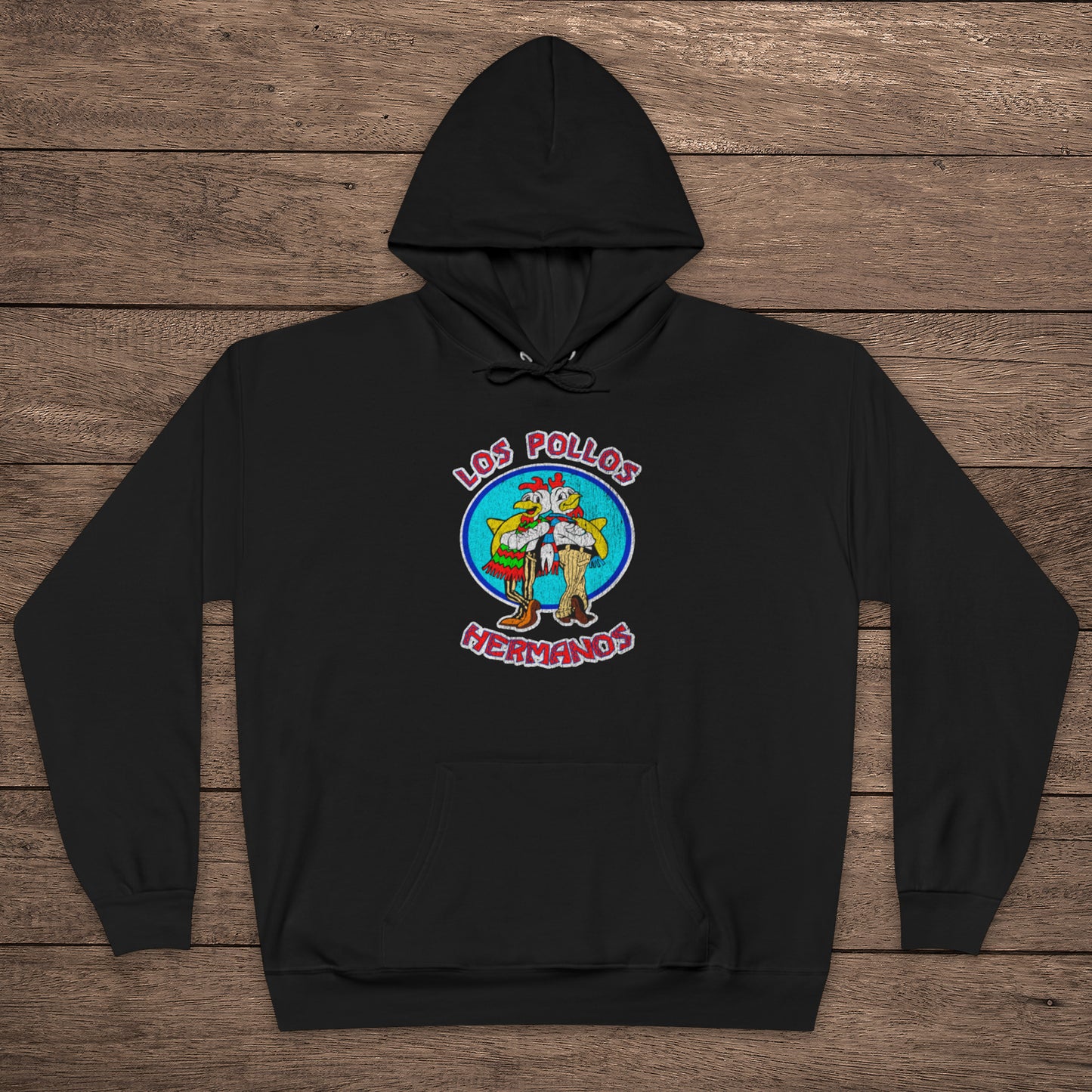 black pullover hoodie with vintage distressed Los Pollos Hermanos logo from Breaking Bad on chest, shown on a wood floor.