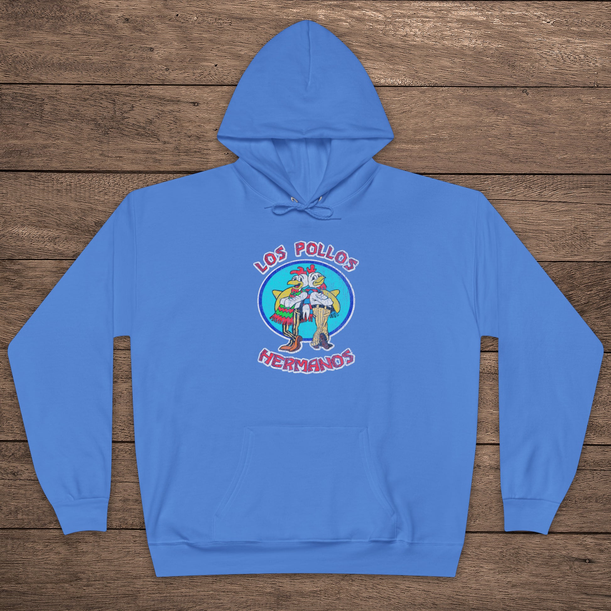 Carolina blue pullover hoodie with vintage distressed Los Pollos Hermanos logo from Breaking Bad on chest, shown on a wood floor.