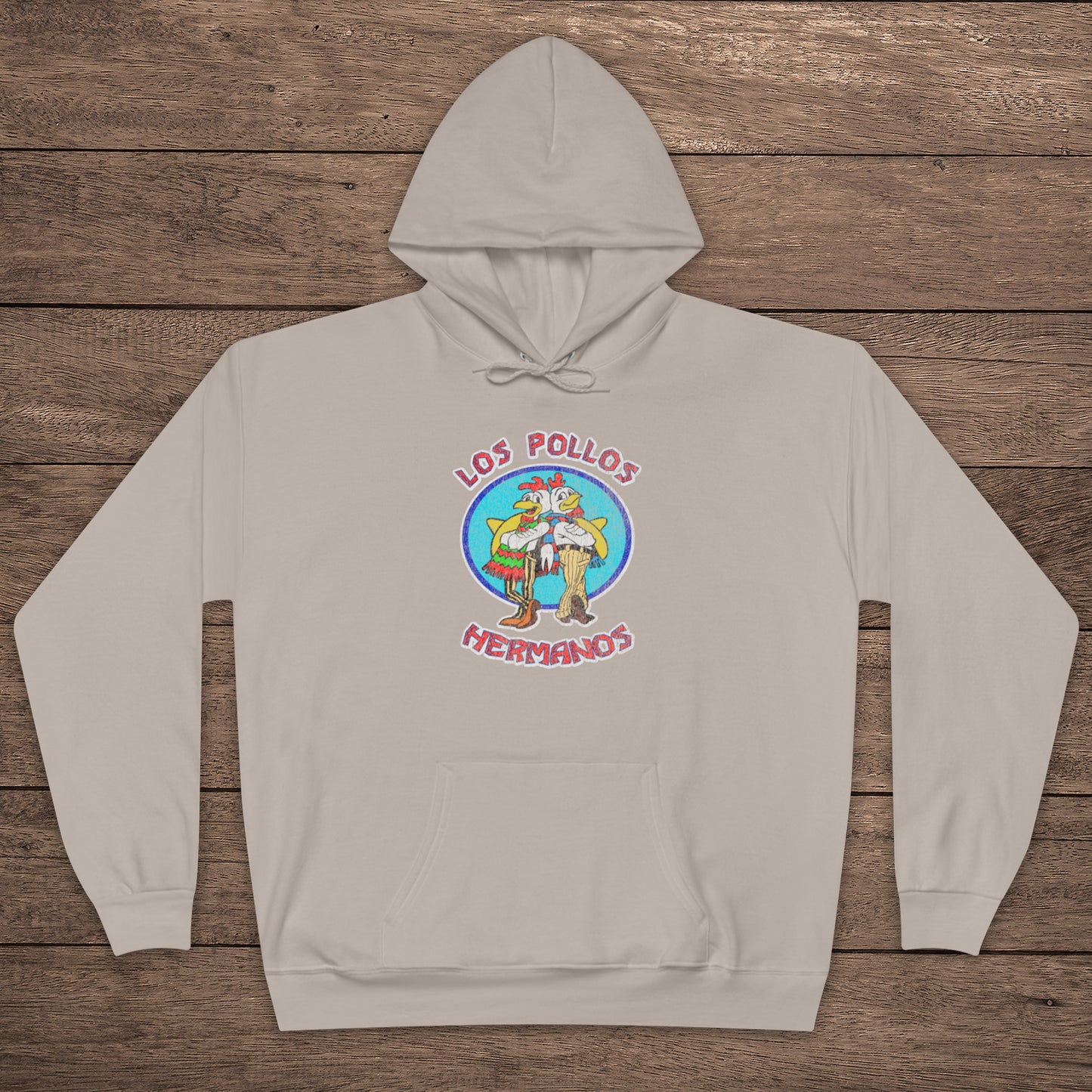 sand beige pullover hoodie with vintage distressed Los Pollos Hermanos logo from Breaking Bad on chest, shown on a wood floor.