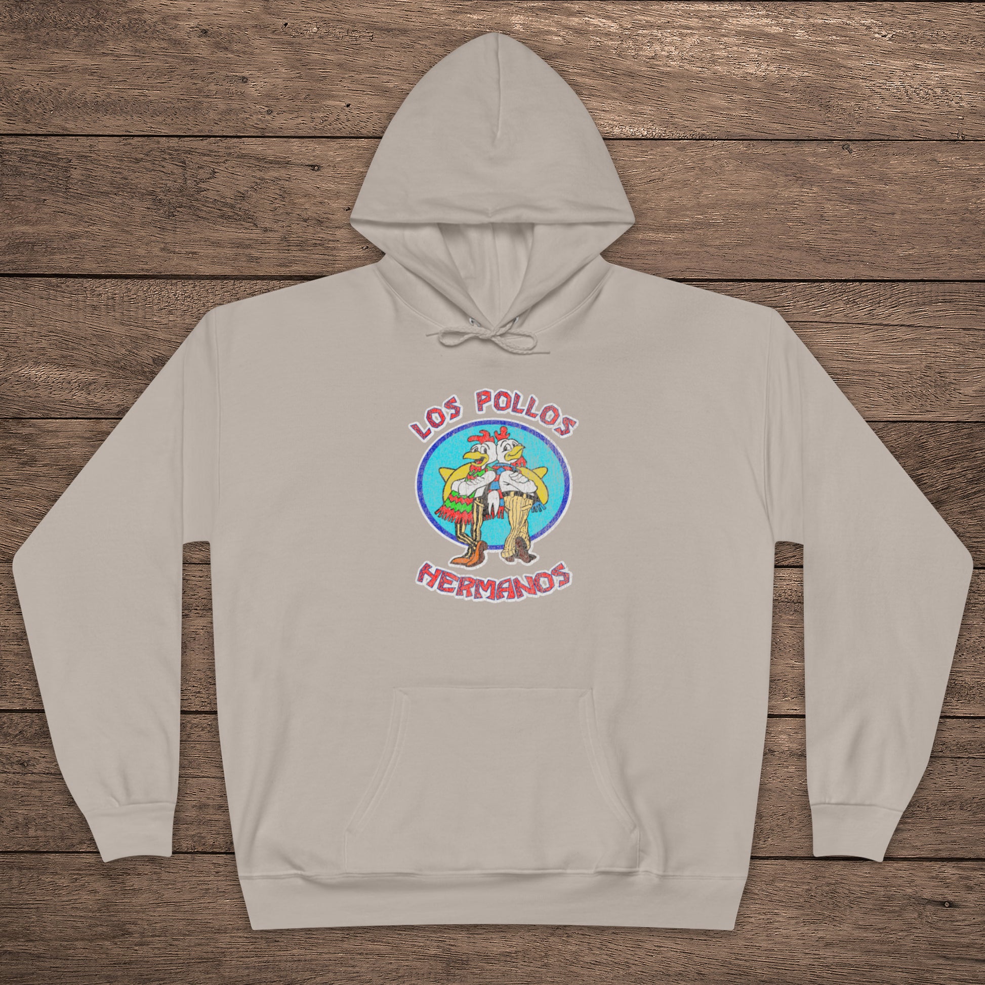 sand beige pullover hoodie with vintage distressed Los Pollos Hermanos logo from Breaking Bad on chest, shown on a wood floor.