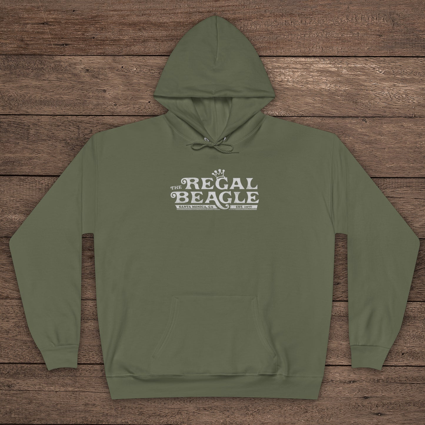 Fatigue Green Hanes EcoSmart pullover hoodie with vintage distressed Regal Beagle logo from Three’s Company on chest, shown on wood floor.