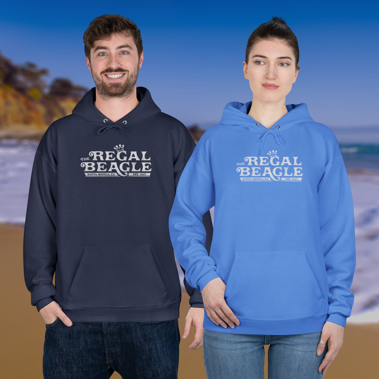 Two people wearing Hanes EcoSmart pullover hoodie with vintage distressed Regal Beagle logo from Three’s Company on chest, standing at a beach.