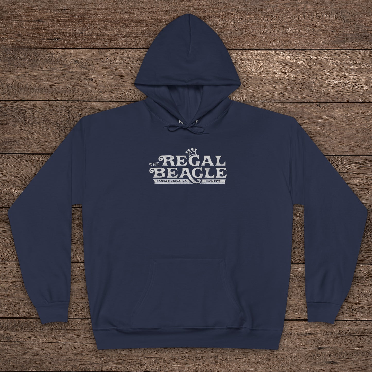 Navy Blue Hanes EcoSmart pullover hoodie with vintage distressed Regal Beagle logo from Three’s Company on chest, shown on wood floor.