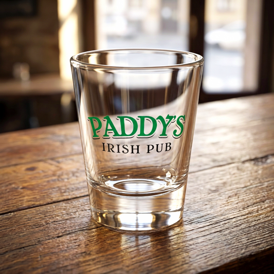 1.5 oz ounce clear shot glass featuring the Paddys Pub logo from the show Its Always Sunny in Philadelphia, on a table in a bar