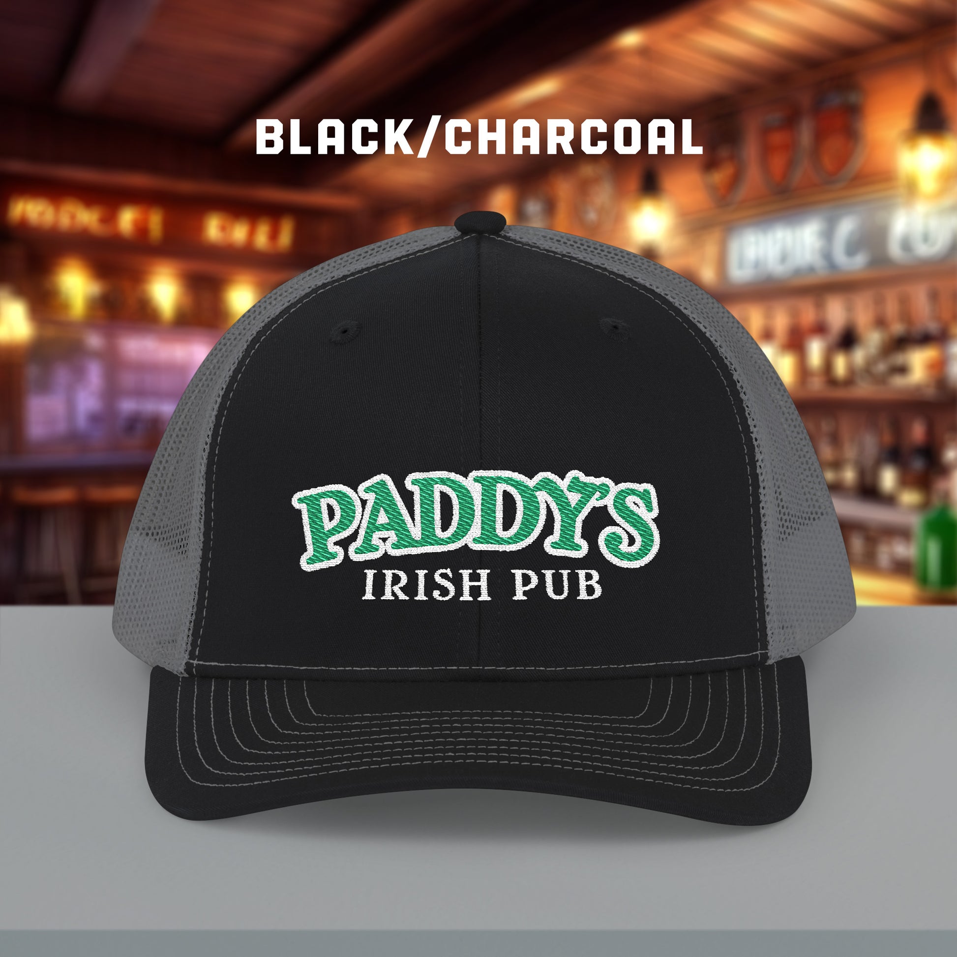 Black charcoal Richardson 112 trucker cap with green Paddy’s Irish Pub embroidered logo shown in a bar.